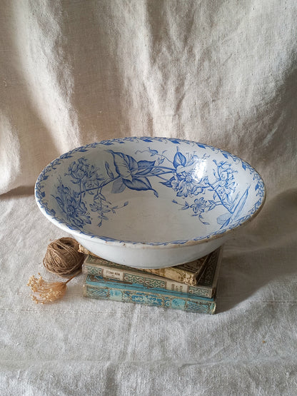 A white ceramic bowl with a blue floral and botanical pattern, styled on top of vintage books with a ball of twine beside it against a draped linen backdrop.