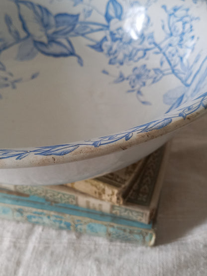 A close-up of a white ceramic bowl with a blue floral pattern, resting on top of vintage books on a white textured fabric surface.