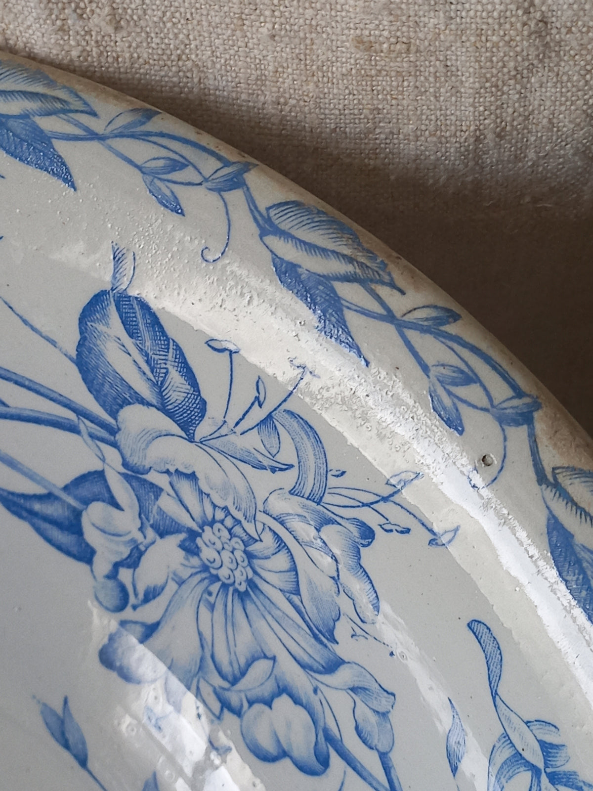 Close-up of a white ceramic bowl with a blue floral and leaf pattern, resting against a textured beige fabric background.