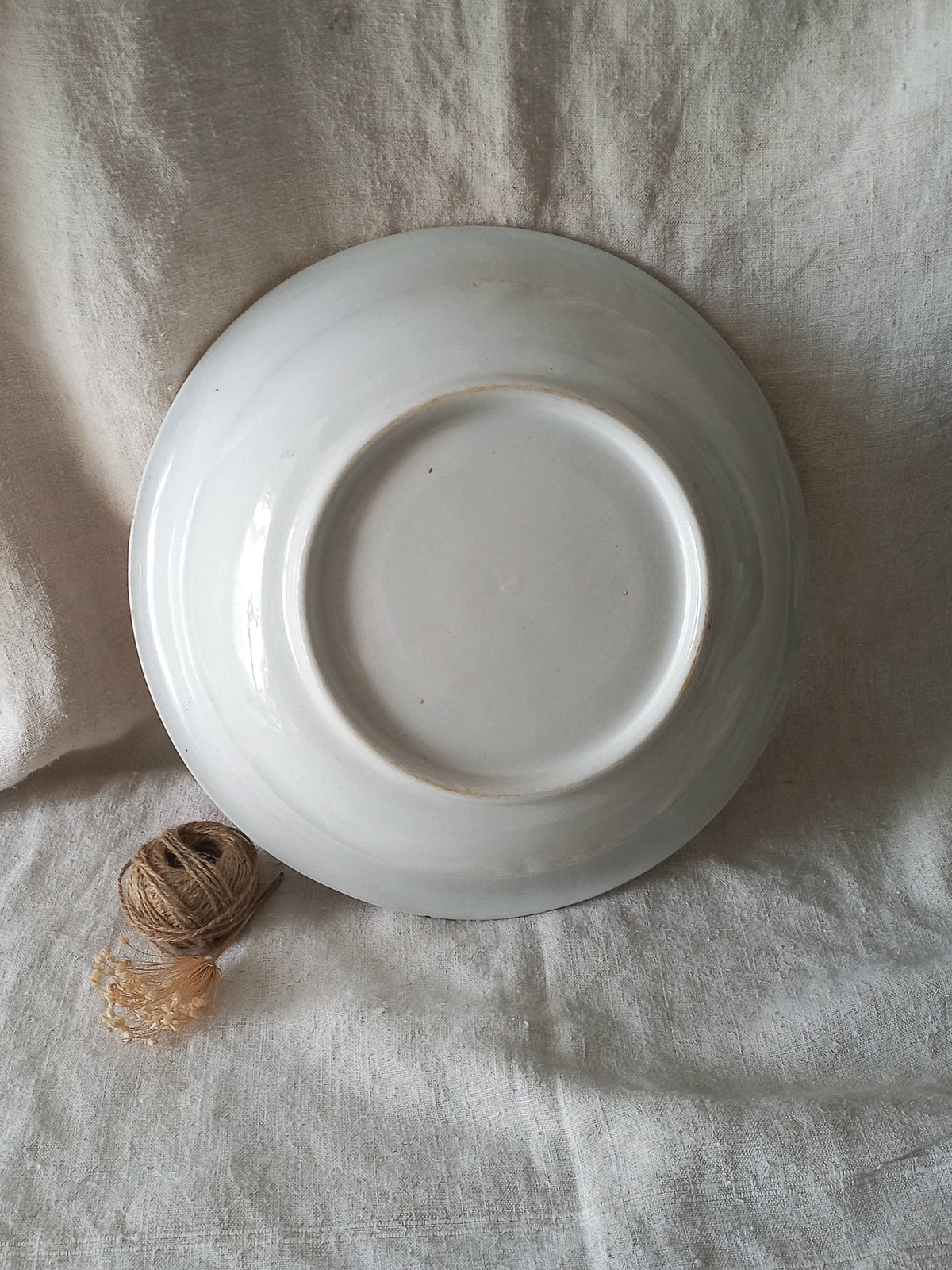 A white ceramic bowl shown from a top-down view, resting on a textured beige linen fabric background with a small ball of twine nearby.