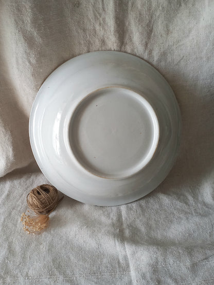 A white ceramic bowl shown from a top-down view, resting on a textured beige linen fabric background with a small ball of twine nearby.