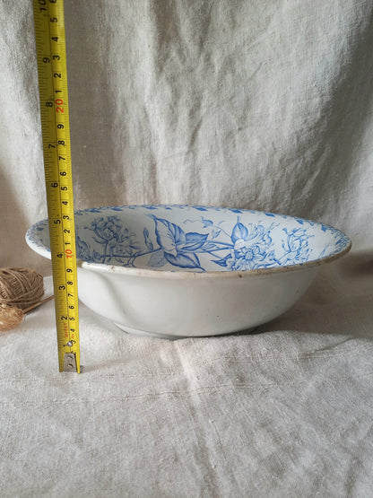 A white ceramic bowl with a blue floral pattern inside, shown next to a yellow tape measure for scale against a draped white linen background.