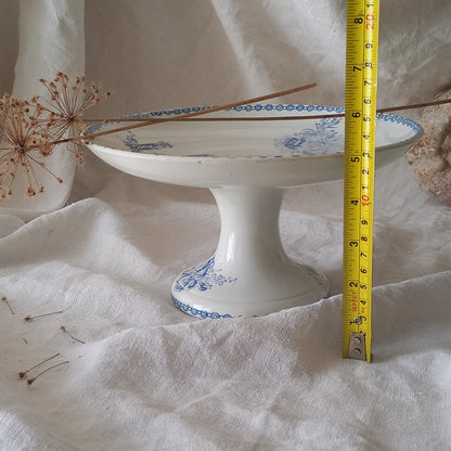 An attractive French antique footed ironstone cake plate with a blue transfer pattern depicting architecture, cherubs, and flowers; a very pretty and delicate pattern.

Original antique ironstone pieces of this age and condition are becoming increasingly difficult to source to this a rare treat to discover.
