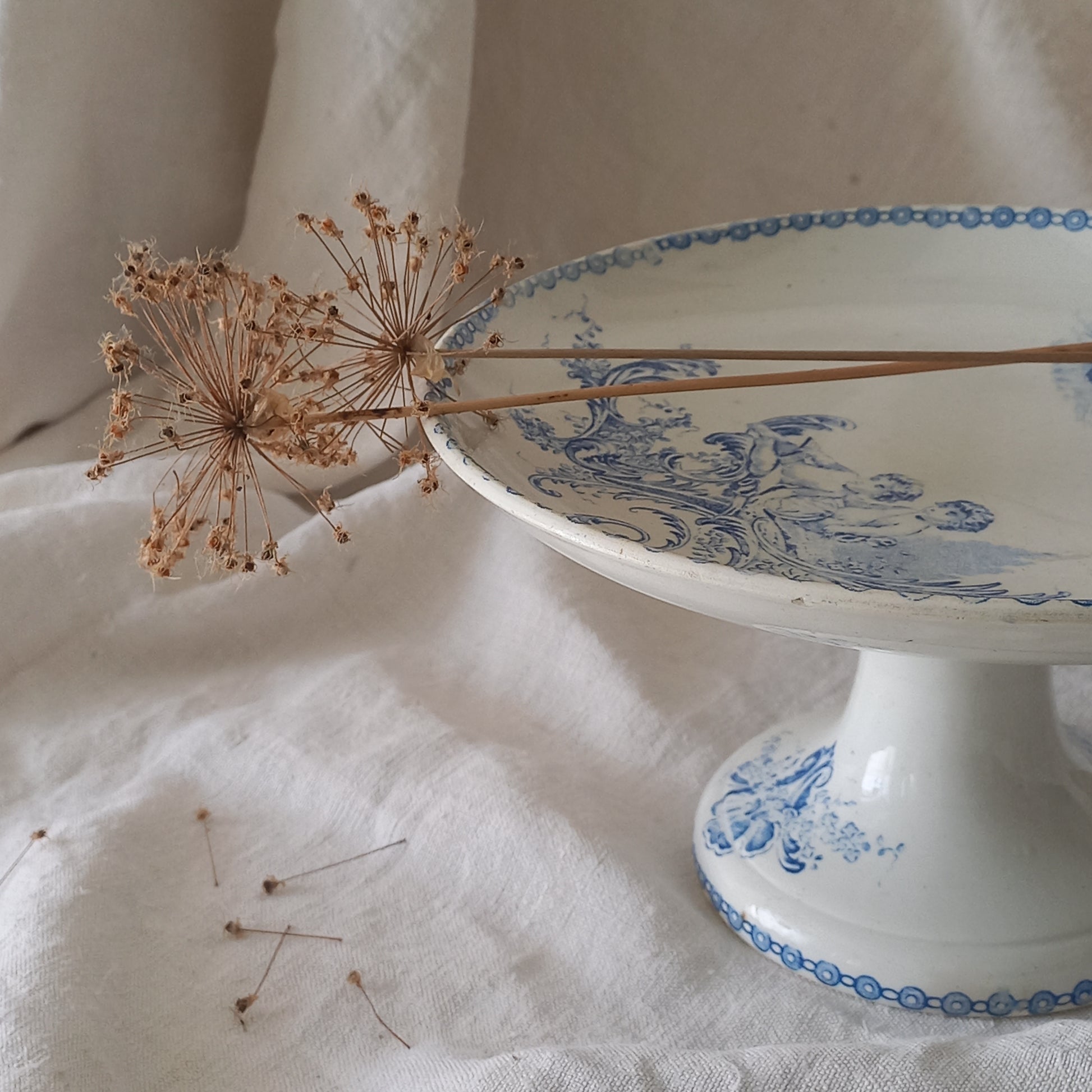 An attractive French antique footed ironstone cake plate with a blue transfer pattern depicting architecture, cherubs, and flowers; a very pretty and delicate pattern.

Original antique ironstone pieces of this age and condition are becoming increasingly difficult to source to this a rare treat to discover.
