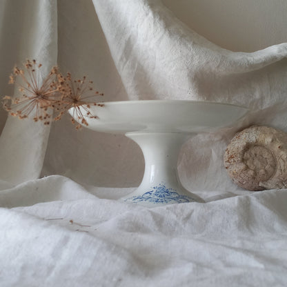 An attractive French antique footed ironstone cake plate with a blue transfer pattern depicting architecture, cherubs, and flowers; a very pretty and delicate pattern.

Original antique ironstone pieces of this age and condition are becoming increasingly difficult to source to this a rare treat to discover.
