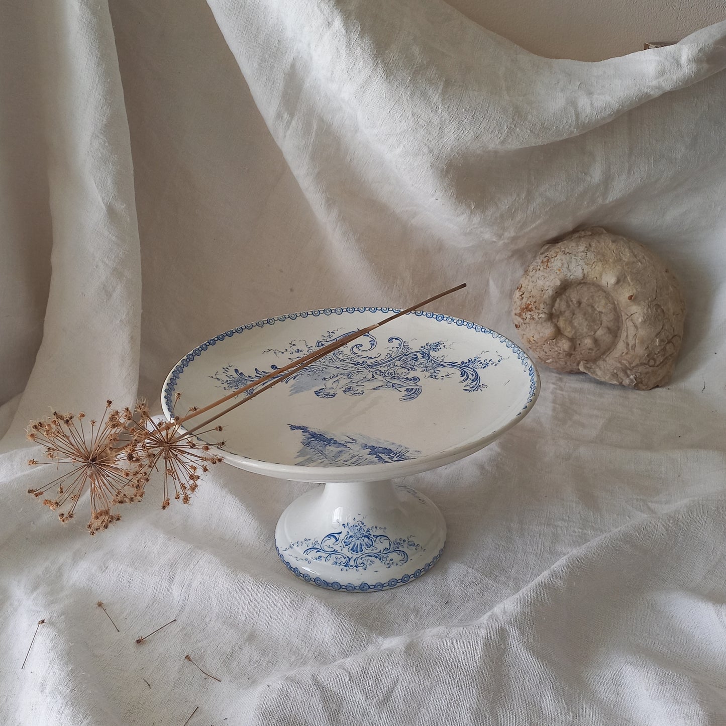 An attractive French antique footed ironstone cake plate with a blue transfer pattern depicting architecture, cherubs, and flowers; a very pretty and delicate pattern.

Original antique ironstone pieces of this age and condition are becoming increasingly difficult to source to this a rare treat to discover.
