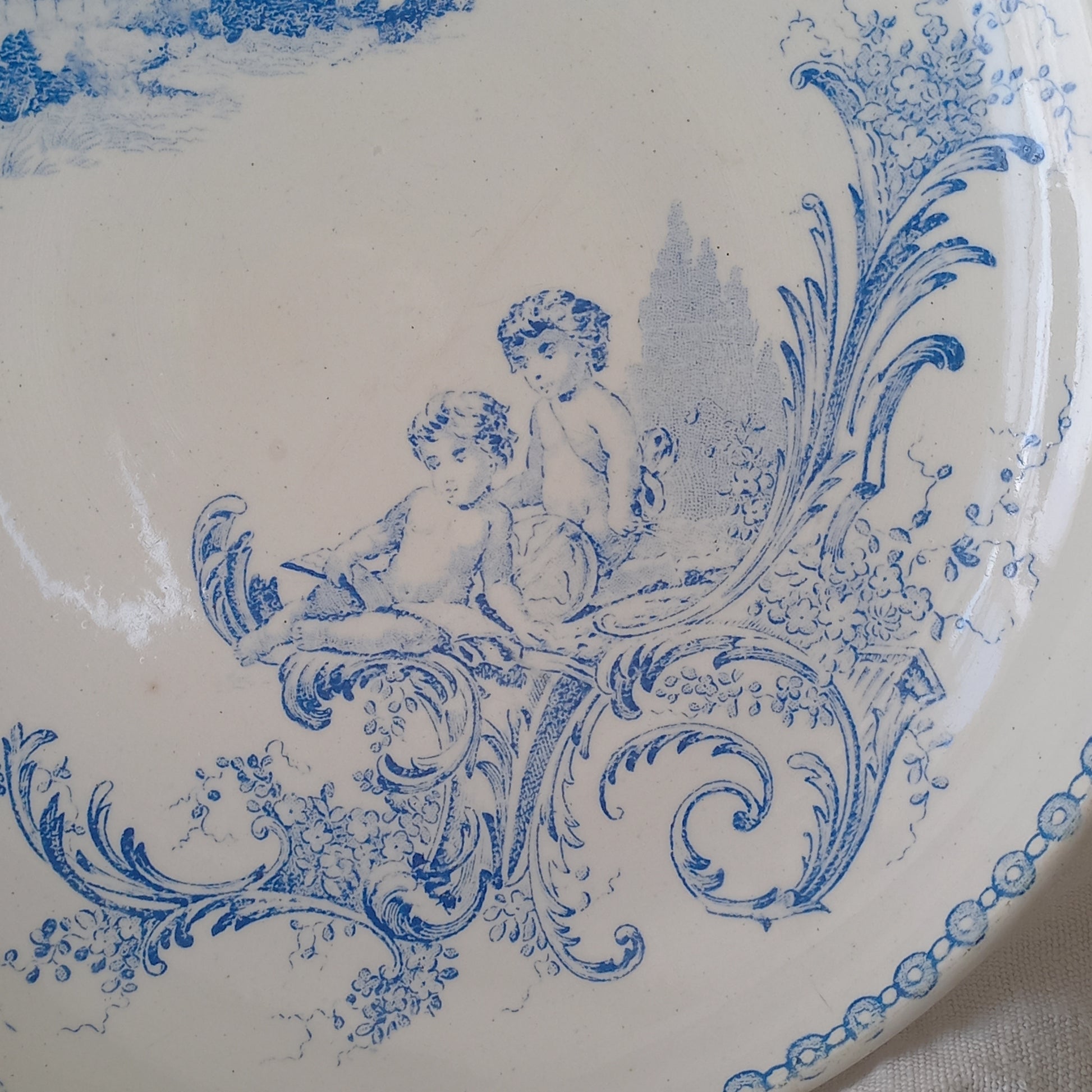 An attractive French antique footed ironstone cake plate with a blue transfer pattern depicting architecture, cherubs, and flowers; a very pretty and delicate pattern.

Original antique ironstone pieces of this age and condition are becoming increasingly difficult to source to this a rare treat to discover.
