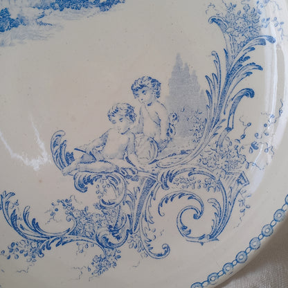 An attractive French antique footed ironstone cake plate with a blue transfer pattern depicting architecture, cherubs, and flowers; a very pretty and delicate pattern.

Original antique ironstone pieces of this age and condition are becoming increasingly difficult to source to this a rare treat to discover.
