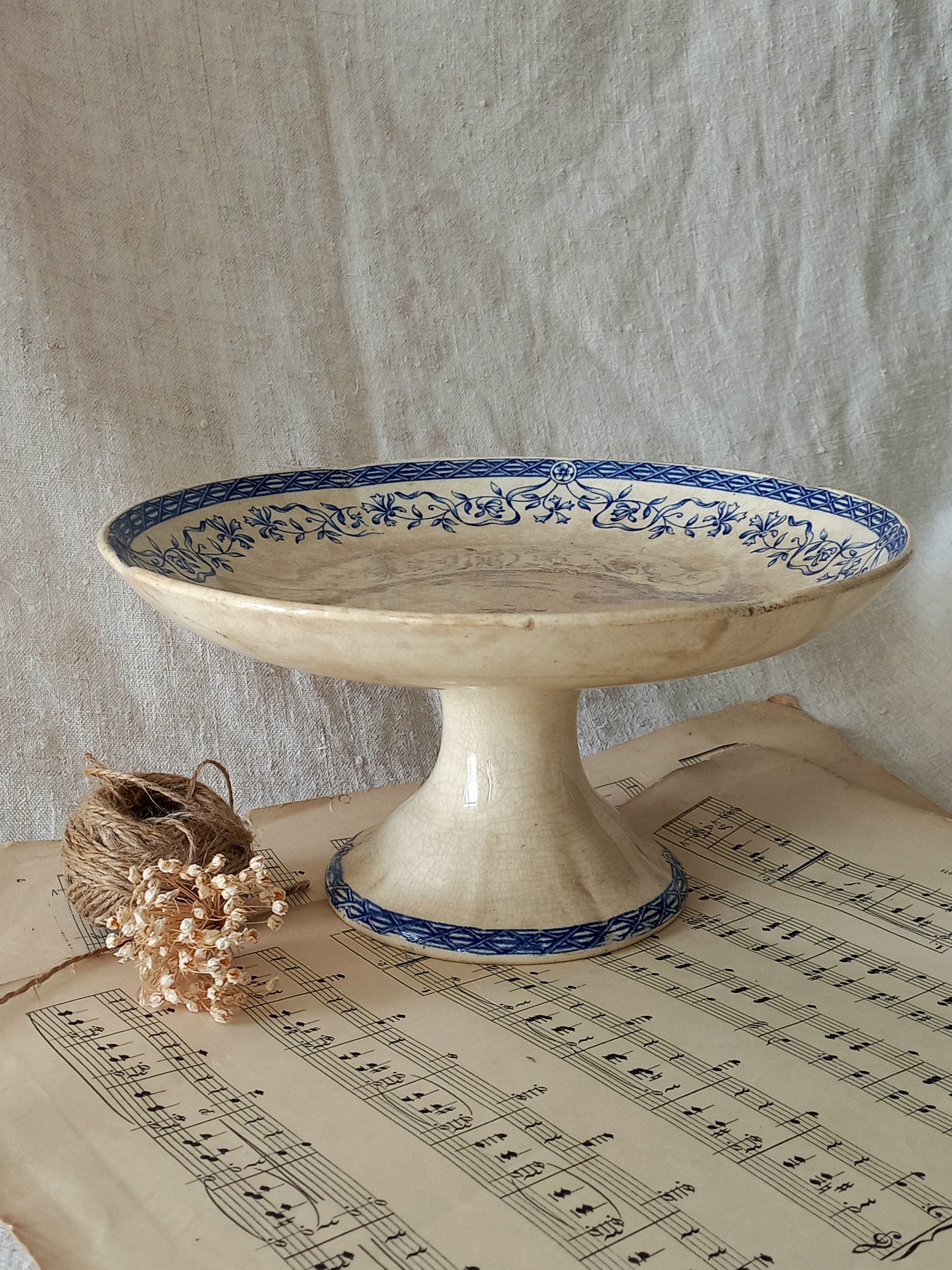 Decorative ceramic pedestal dish with blue floral patterns on a sheet of music.