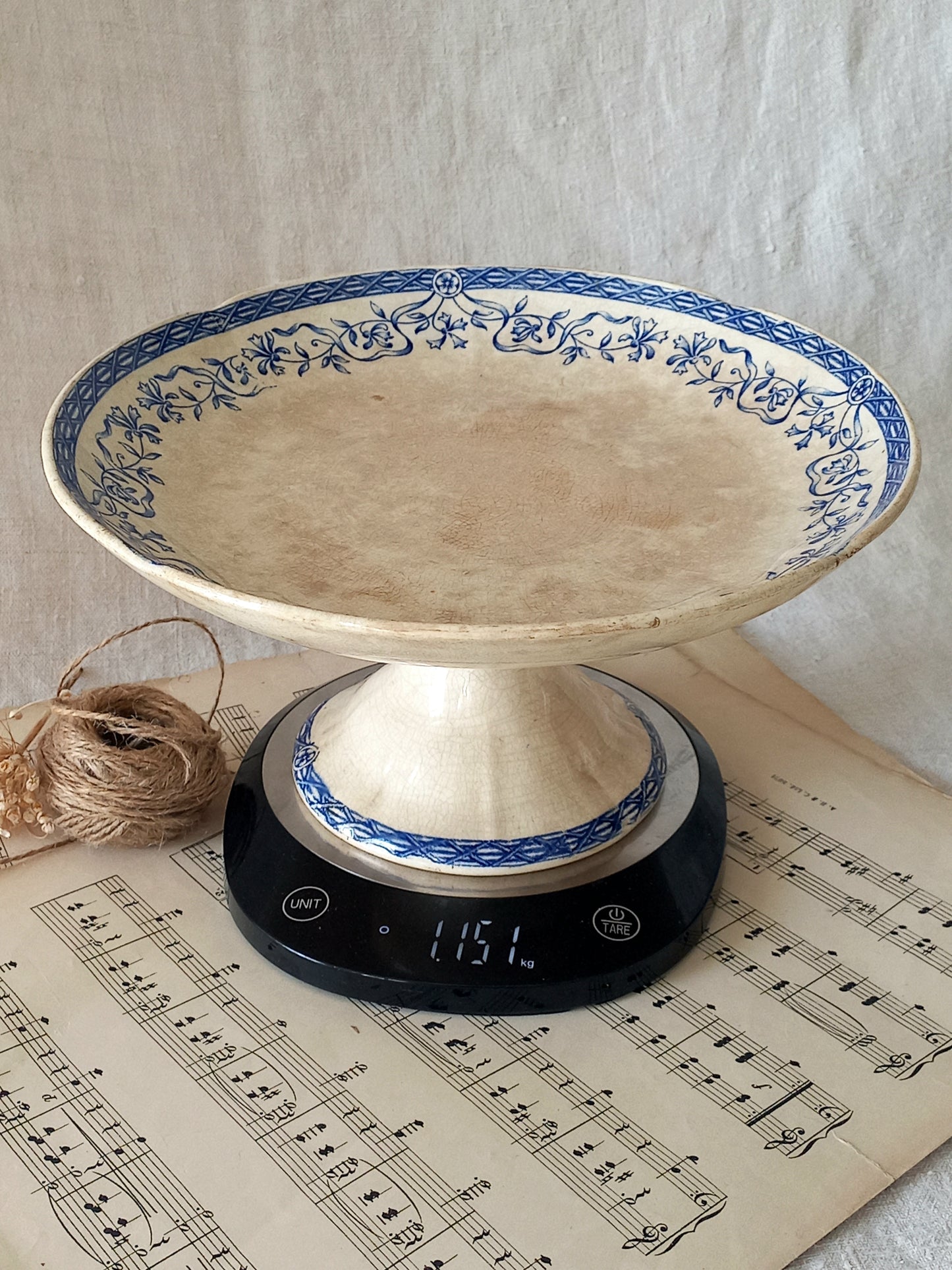 Decorative cake stand with blue floral patterns on a digital kitchen scale over sheet music.