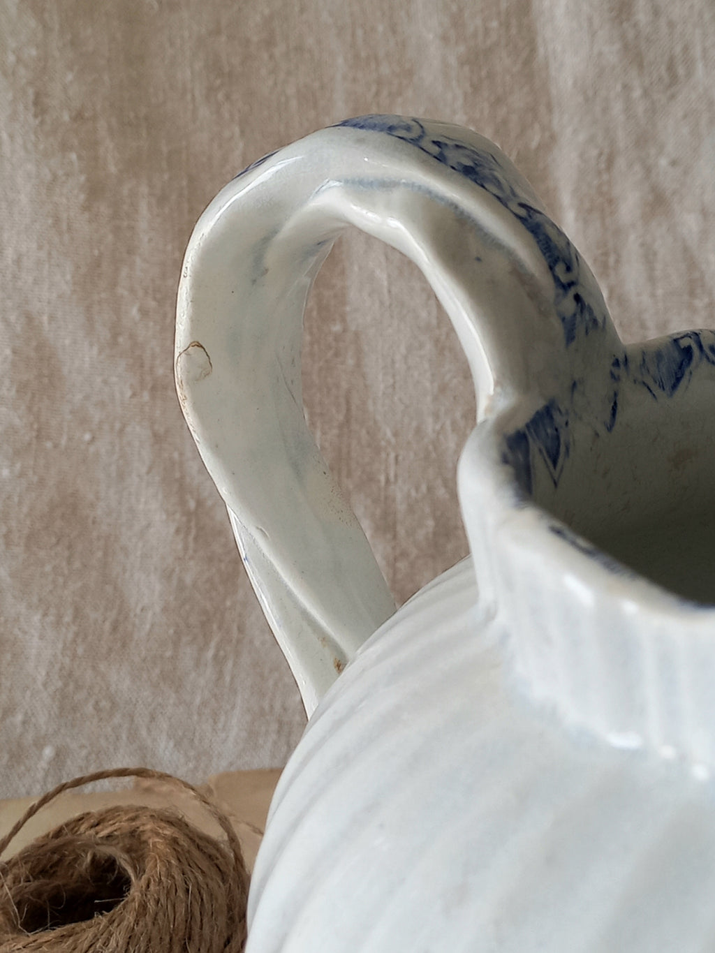 White ceramic pitcher with blue patterns on a textured beige background