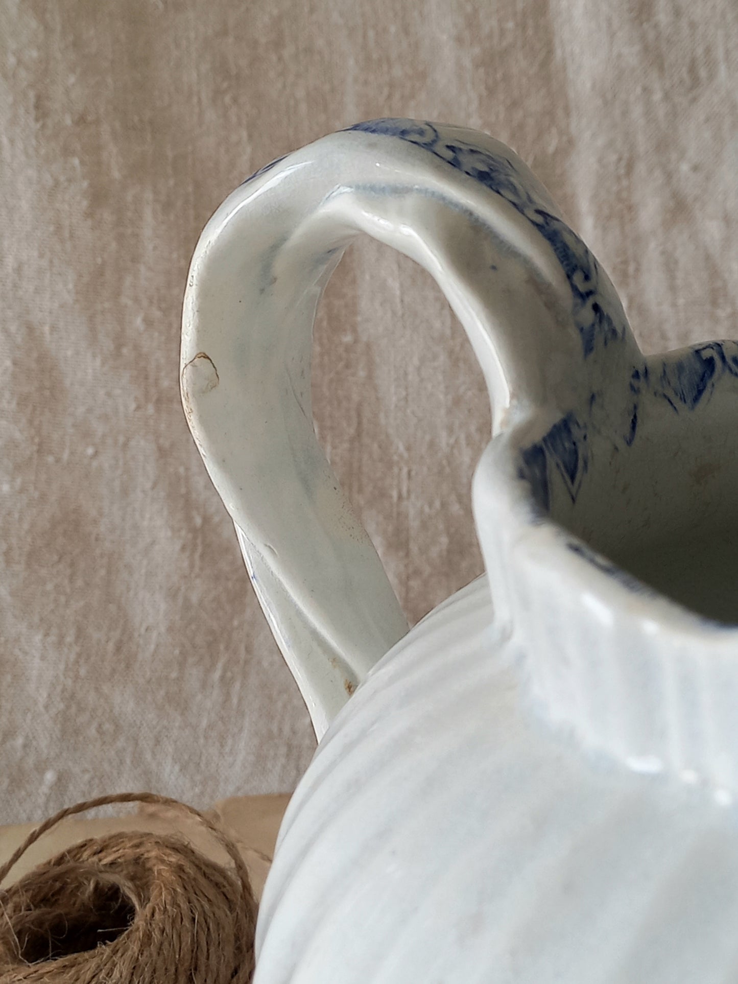 White ceramic pitcher with blue patterns on a textured beige background