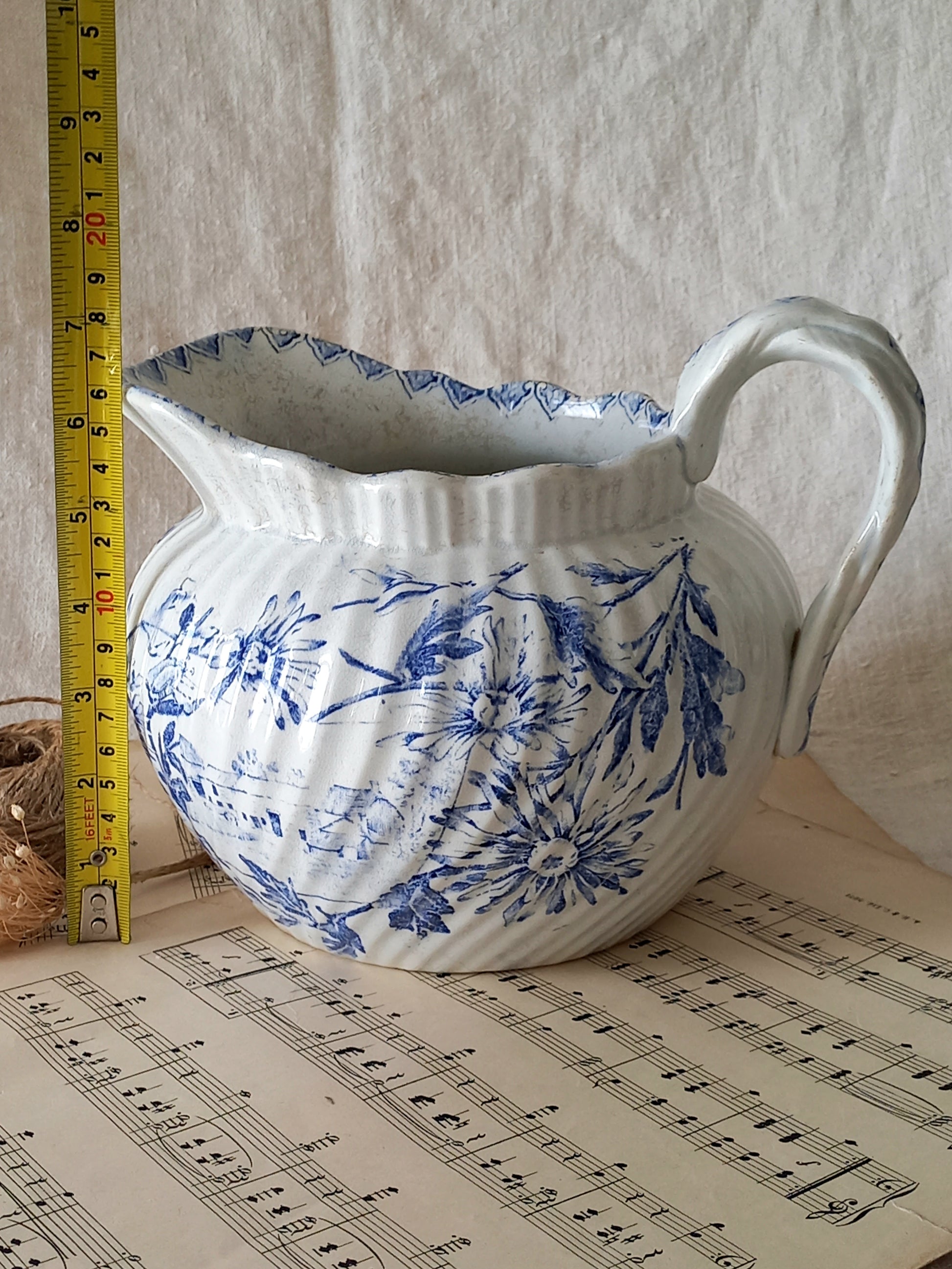 White ceramic pitcher with blue floral pattern on sheet music, with a ruler for scale.