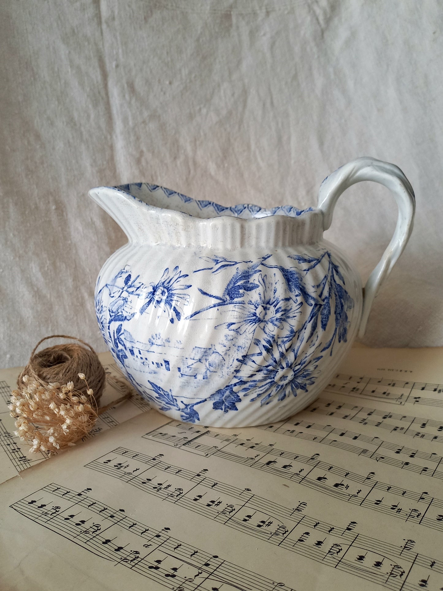 White ceramic pitcher with blue floral patterns on a sheet of music