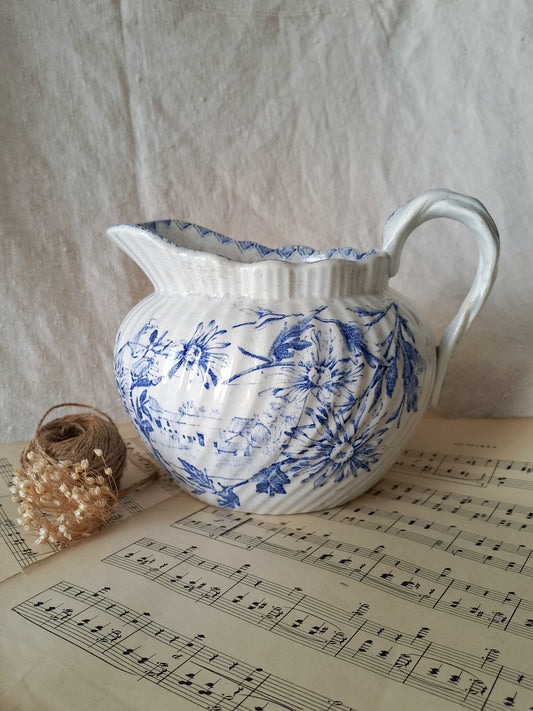 White ceramic pitcher with blue floral patterns on a sheet of music