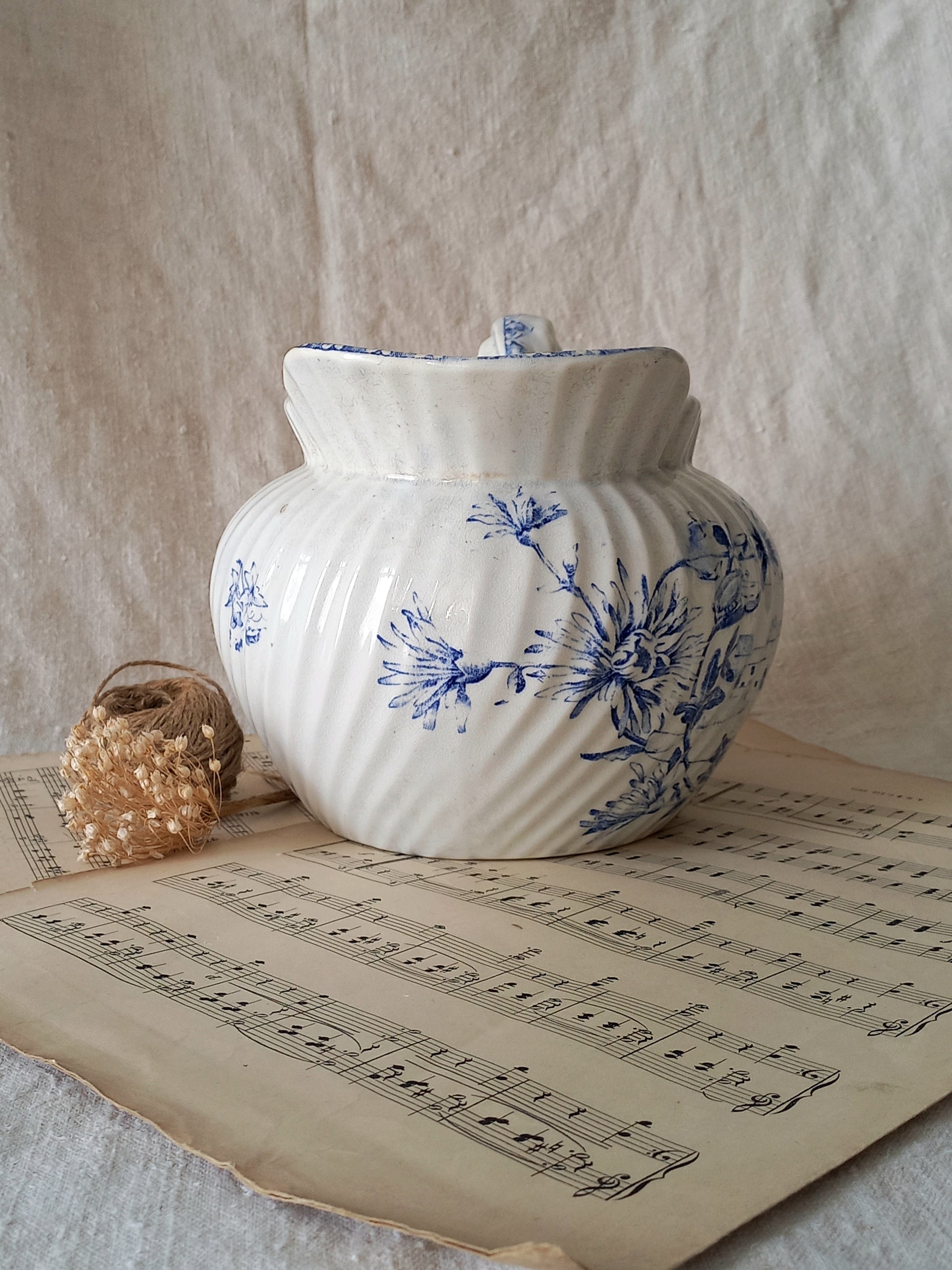 White ceramic jug with blue floral patterns on a sheet of music, against a textured beige background