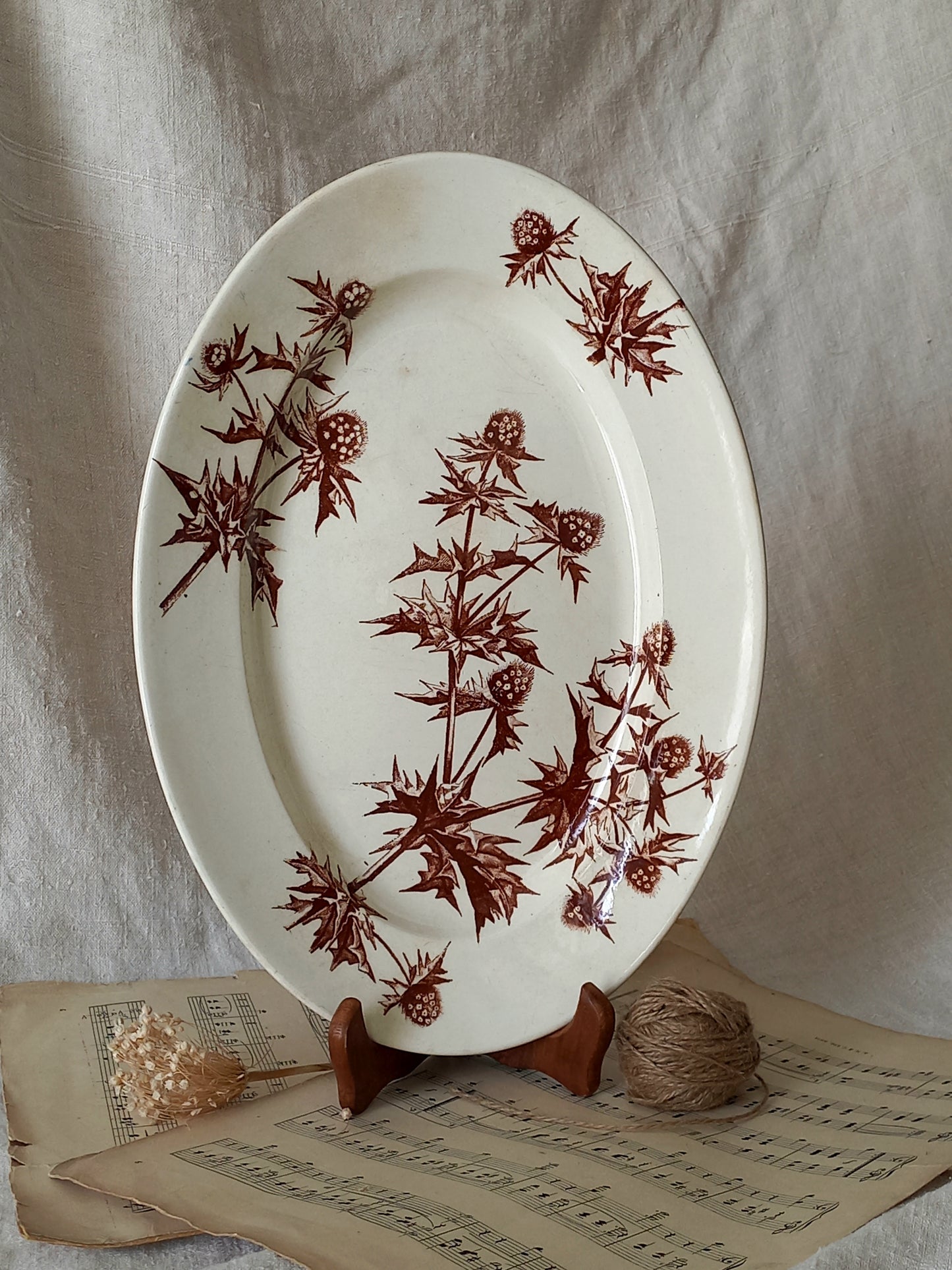 Oval ceramic plate with brown floral pattern on a stand, placed on sheet music.