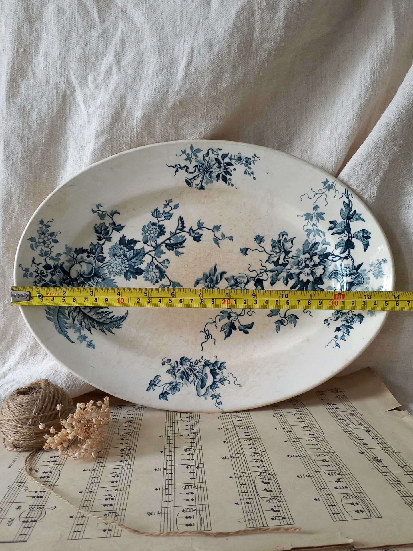 Decorative plate with blue floral patterns on a sheet of music, with a measuring tape for scale.