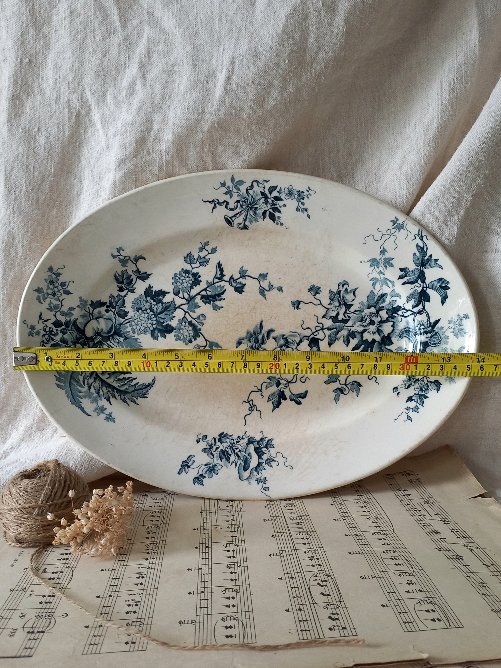 Decorative plate with blue floral patterns on a sheet of music, with a measuring tape for scale.