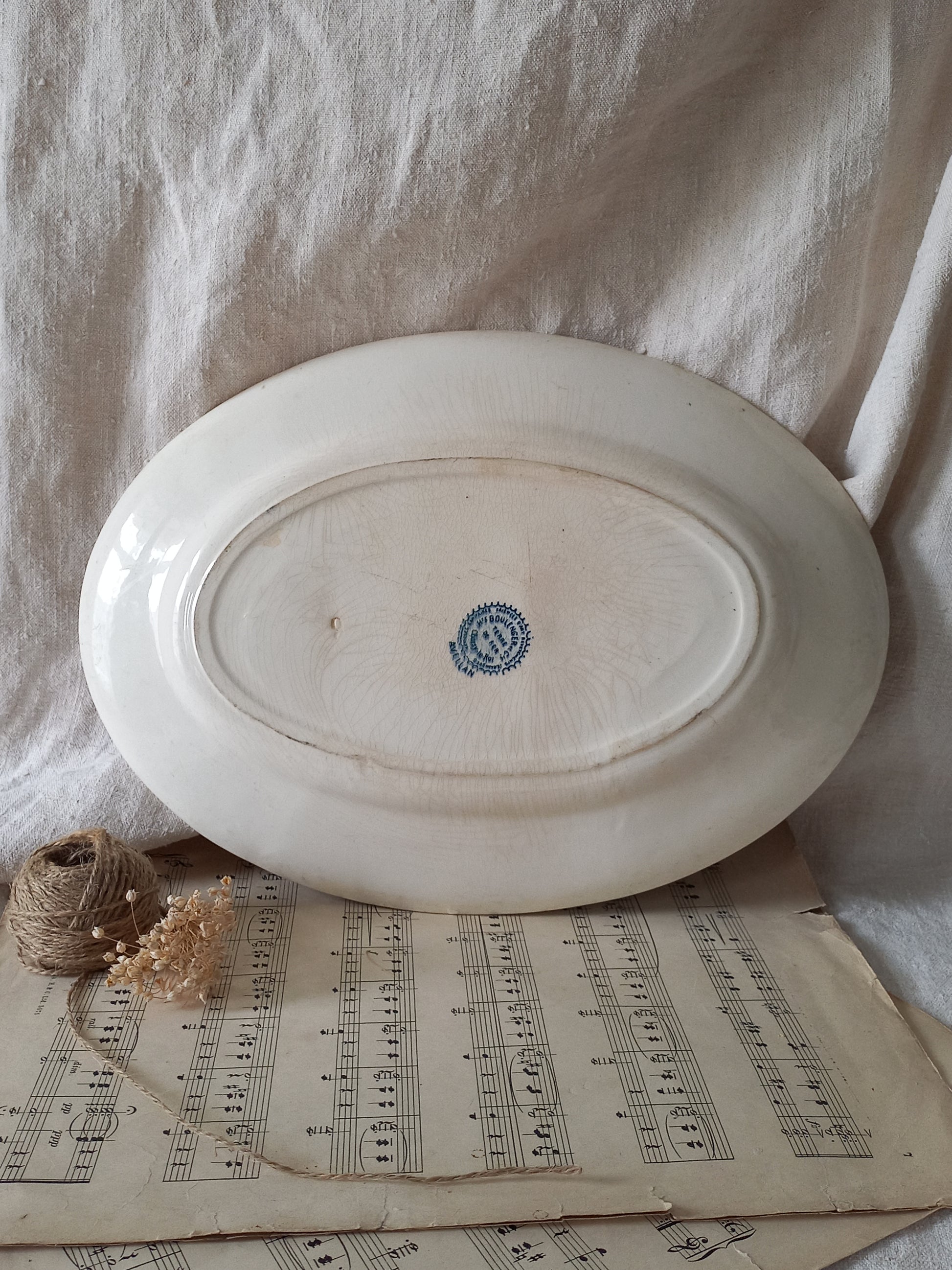White ceramic plate with a blue logo on a surface with sheet music and a small plant.
