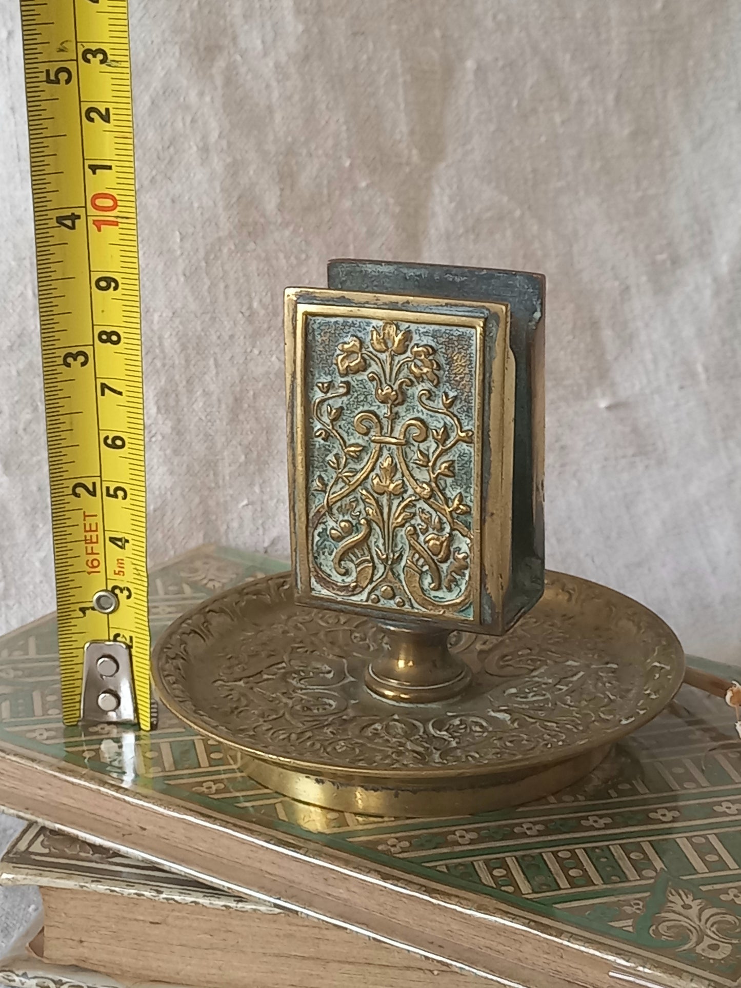 French antique decorative brass-coated matchbox holder in a decorative setting with a tape measure for reference.