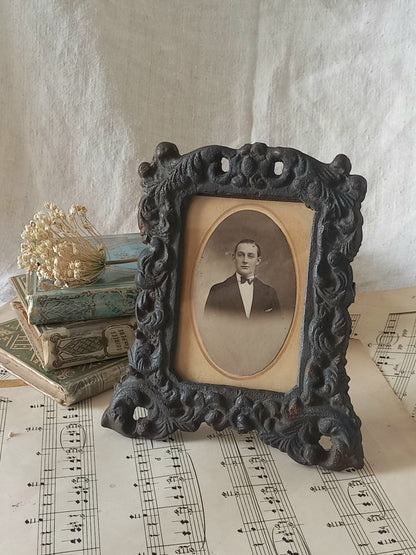 A small French antique decorative cast iron photo frame with time-worn patina. There is a glass front and a hardboard backing board. Inside is an original period photo.