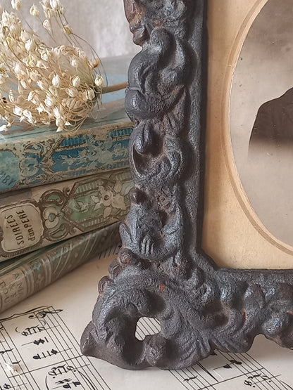 A small French antique decorative cast iron photo frame with time-worn patina. There is a glass front and a hardboard backing board. Inside is an original period photo.