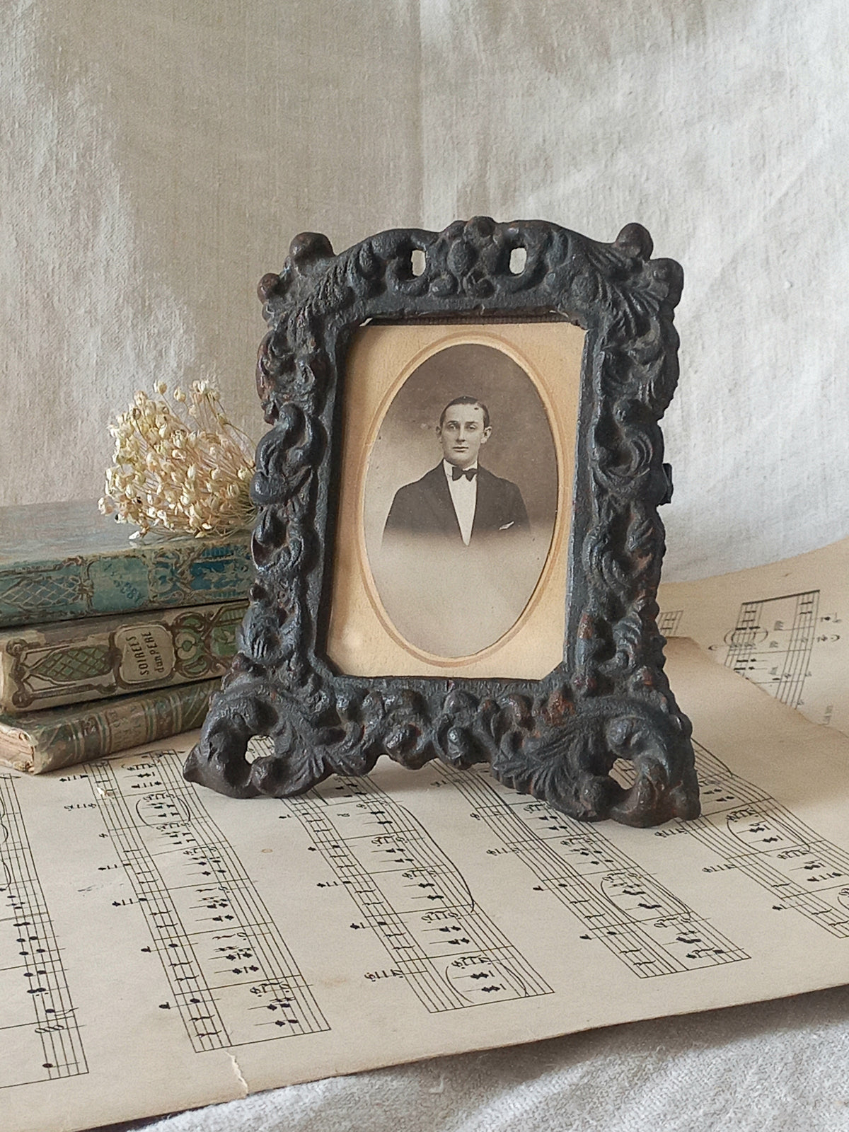 A small French antique decorative cast iron photo frame with time-worn patina. There is a glass front and a hardboard backing board. Inside is an original period photo.