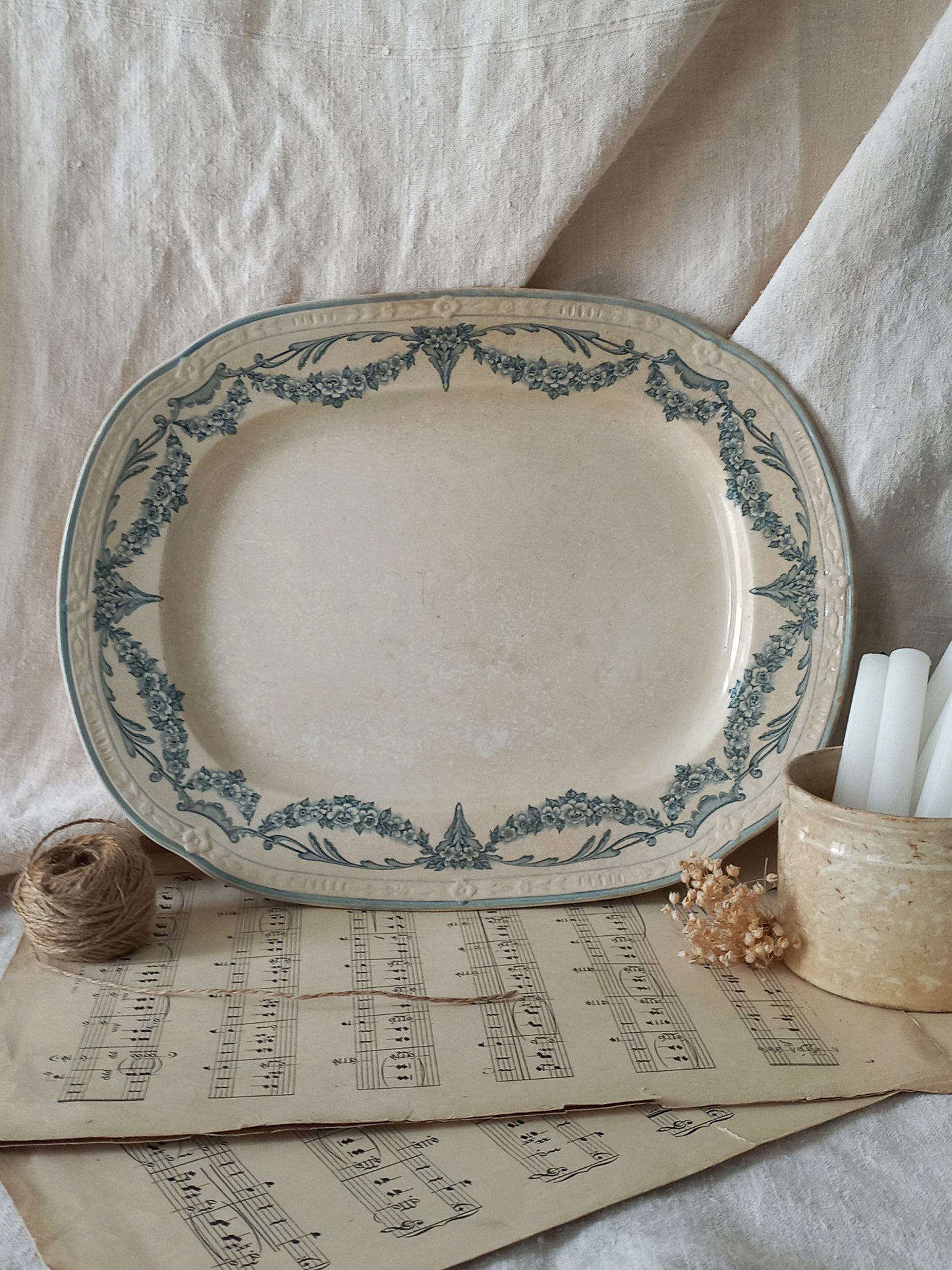 Decorative ceramic platter with blue floral patterns on a surface with sheet music and candles.