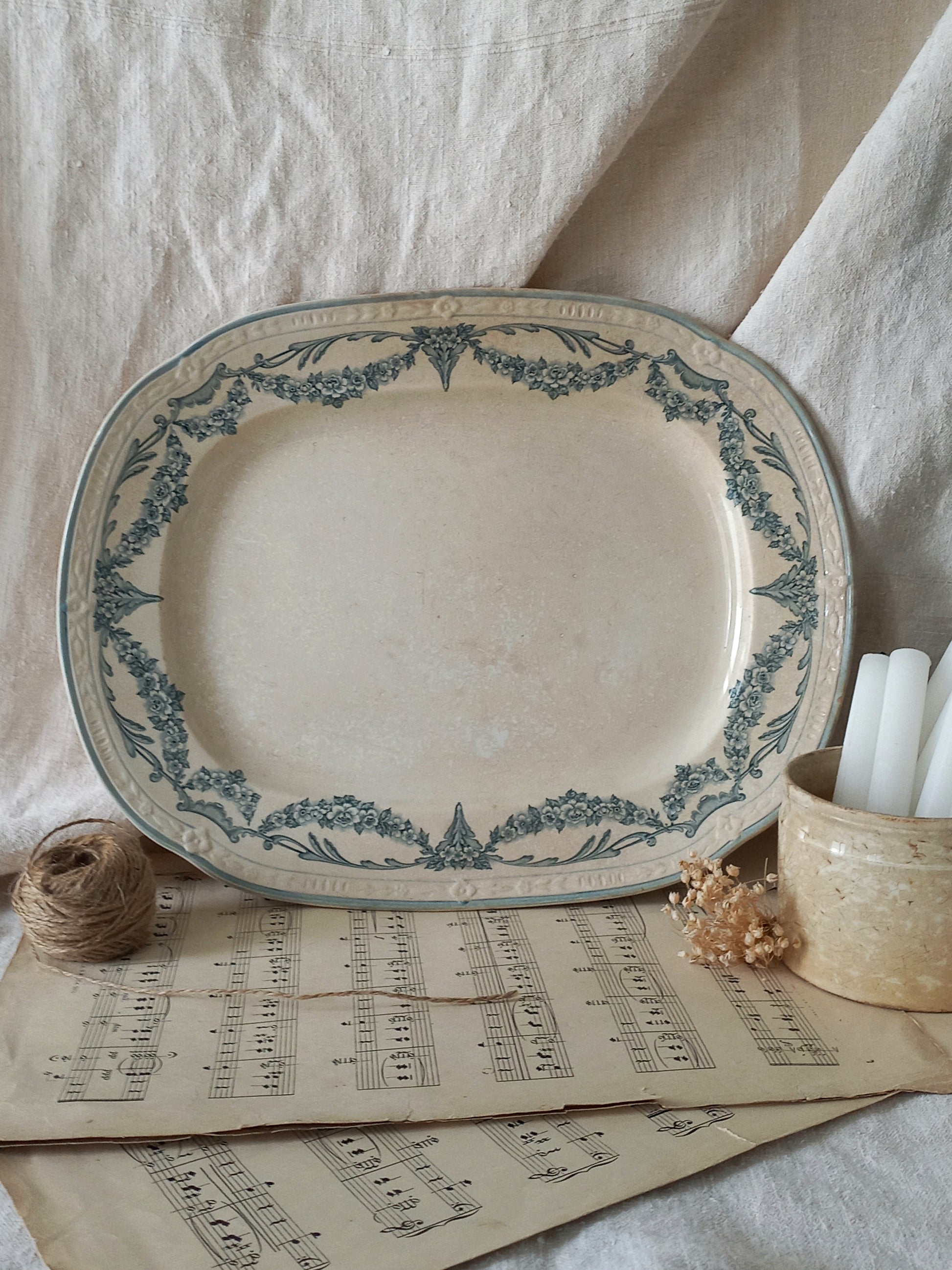 Decorative ceramic platter with blue floral patterns on a surface with sheet music and candles.