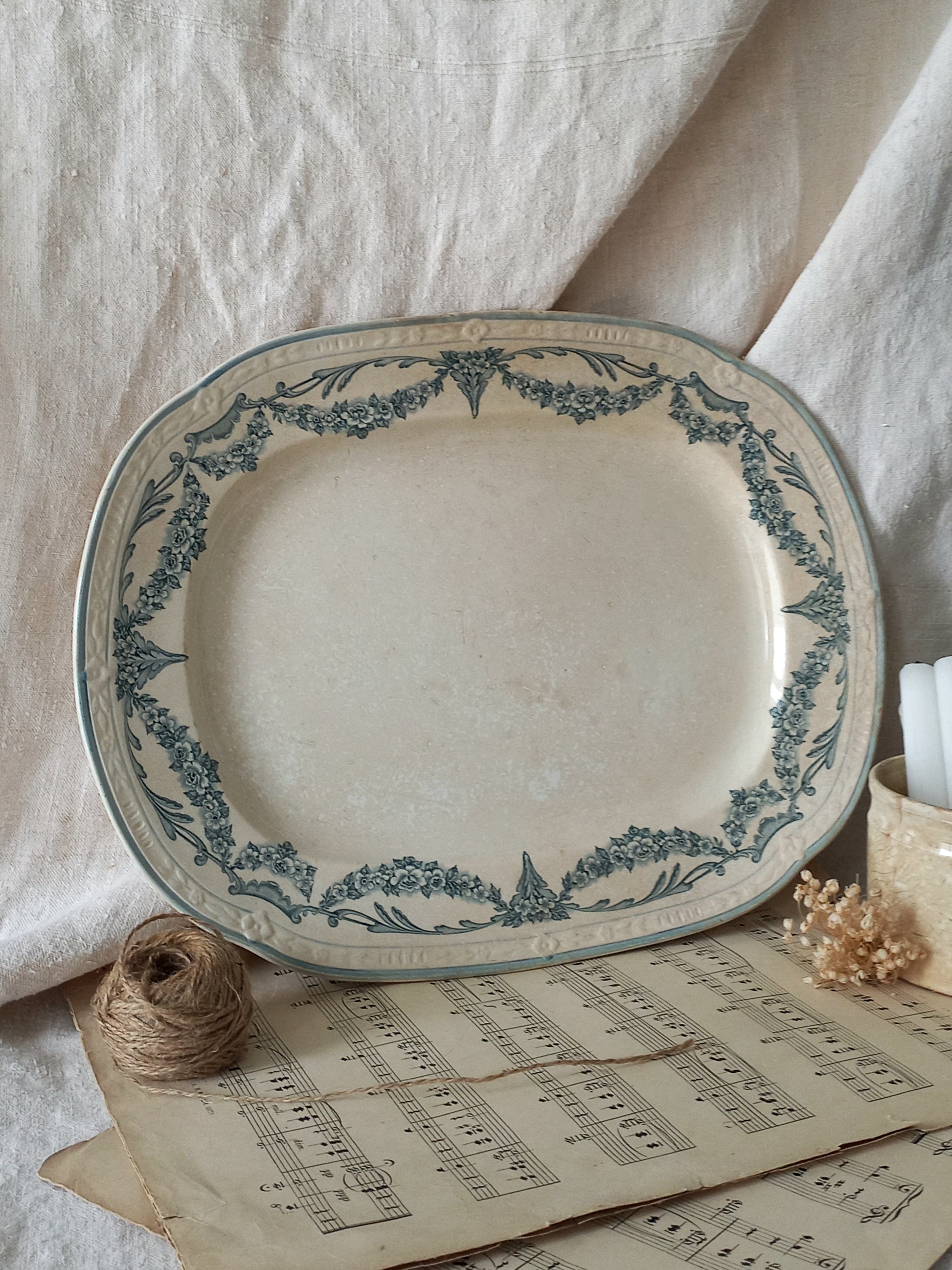 Decorative ceramic platter with blue floral patterns on a surface with old music sheets and twine.