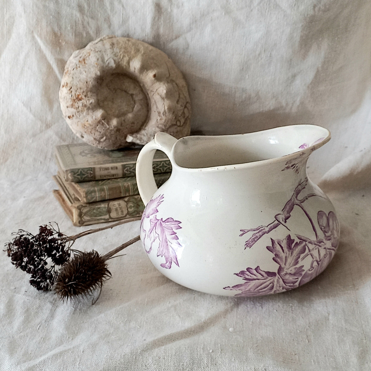 White ceramic pitcher with purple floral patterns on a textured white surface with books and a stone.