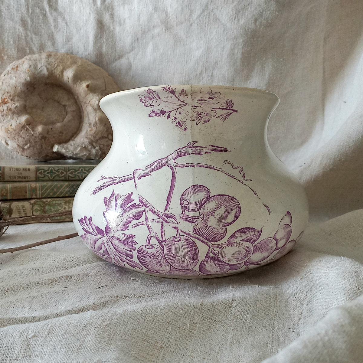 White ceramic vase with purple floral design on a textured fabric background