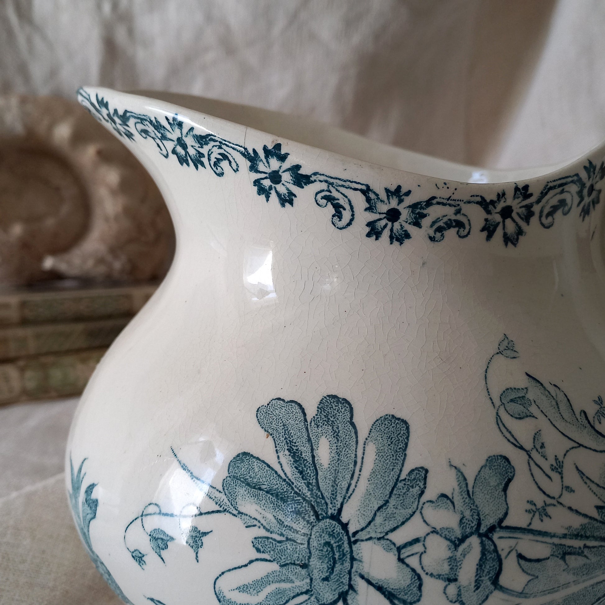 White ceramic pitcher with teal floral patterns on a neutral background