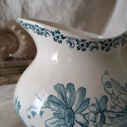 White ceramic pitcher with teal floral patterns on a neutral background