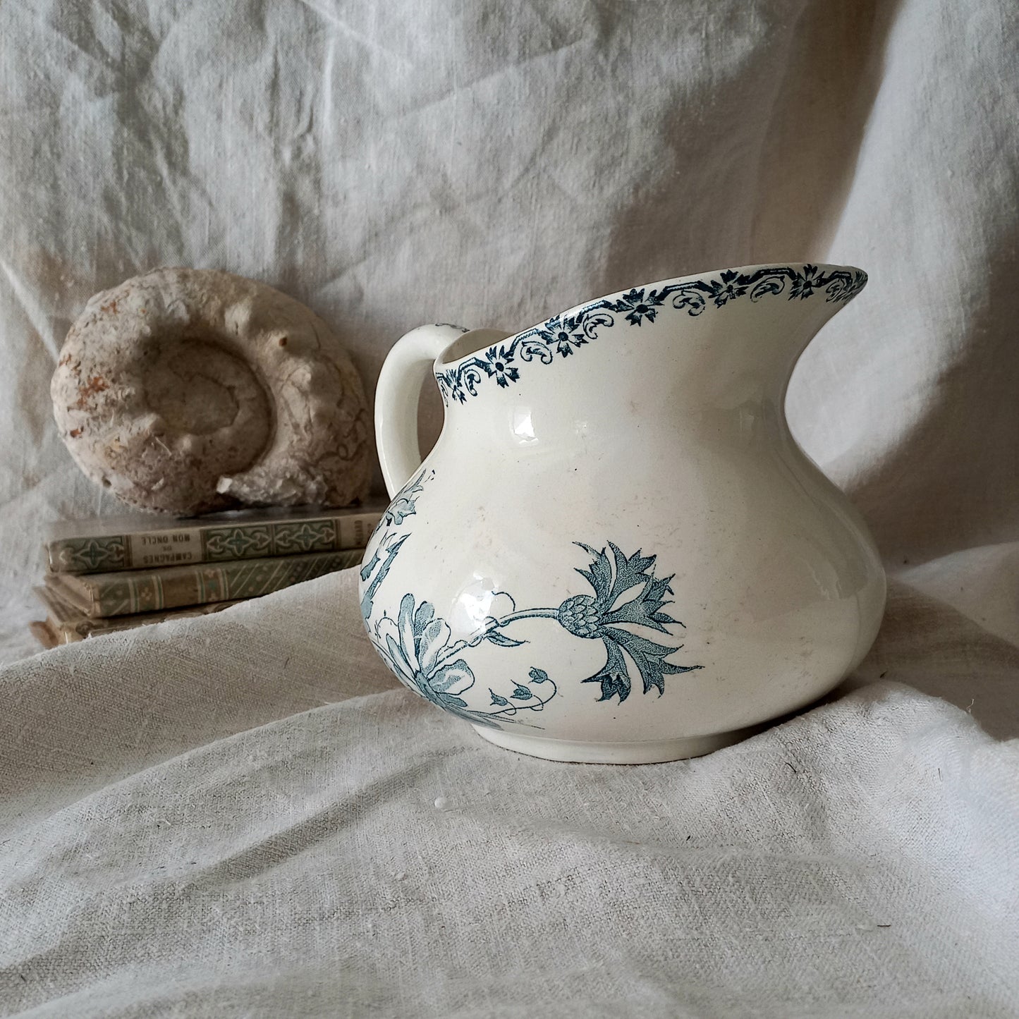 White ceramic pitcher with teal floral patterns on a textured fabric background