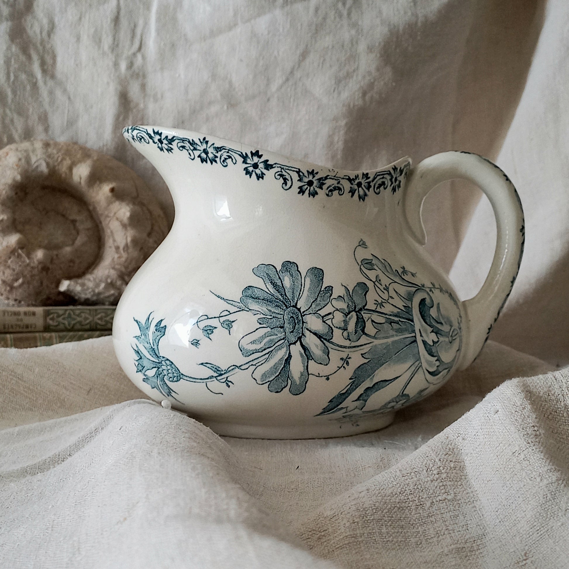 White ceramic pitcher with teal floral patterns on a textured fabric background