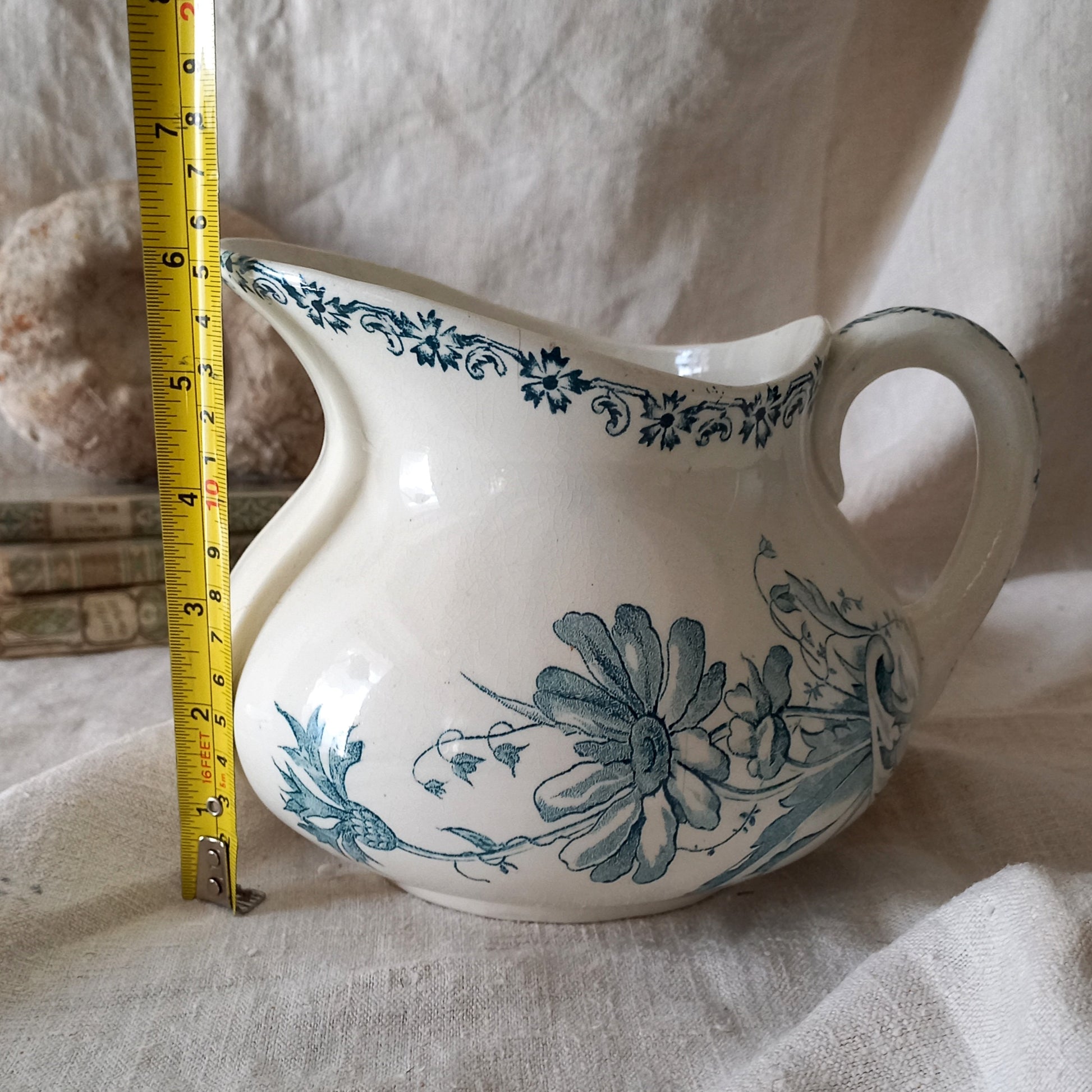 Ceramic pitcher with floral design on a textured surface, measured by a tape measure.
