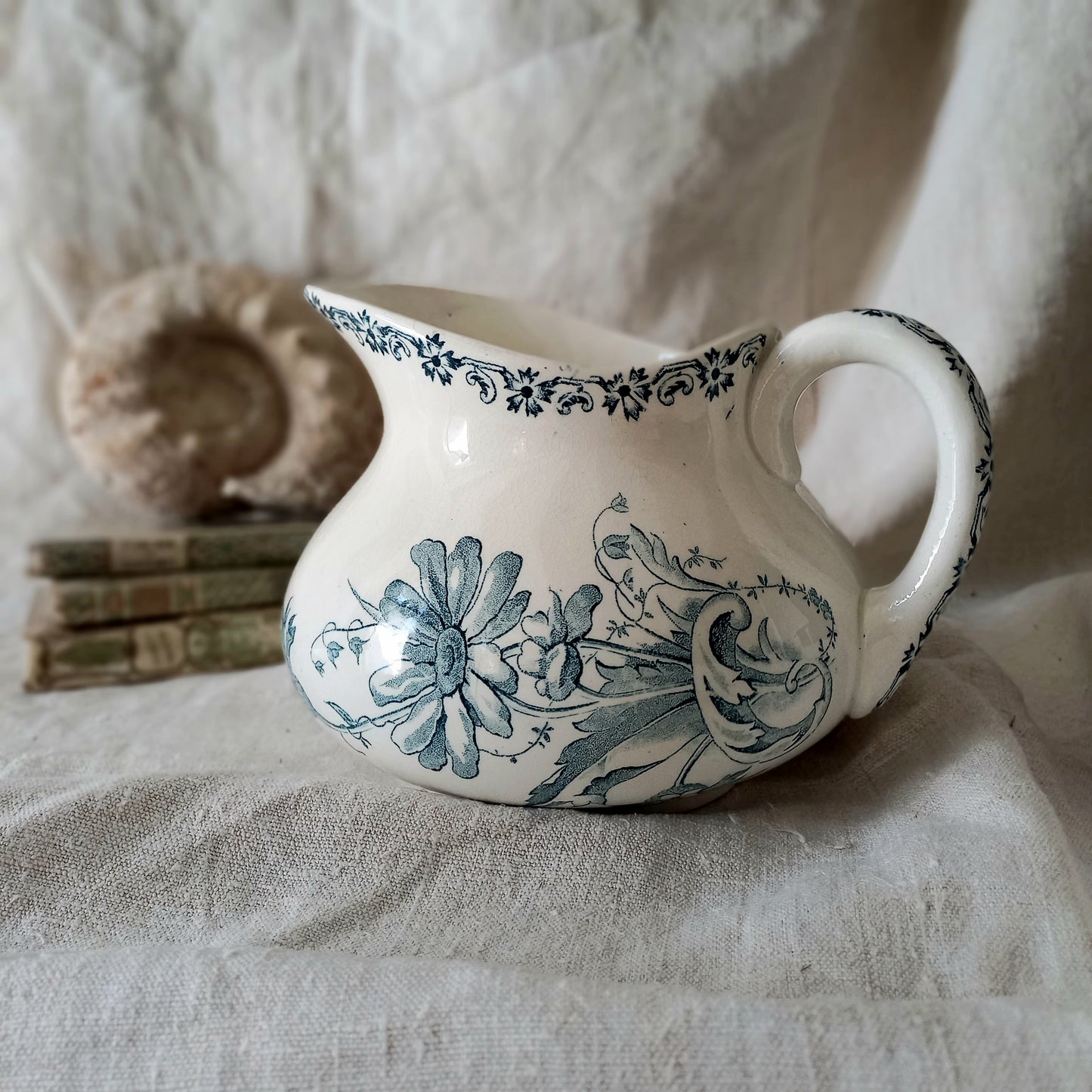 White ceramic pitcher with teal floral patterns on a textured fabric background