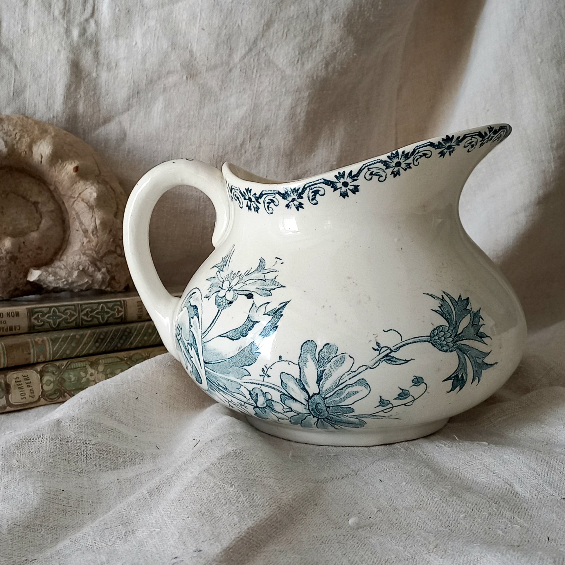 White ceramic pitcher with teal floral patterns on a textured surface
