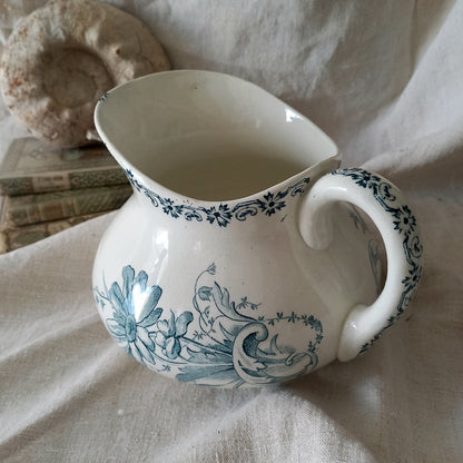 White ceramic pitcher with teal floral patterns on a textured surface