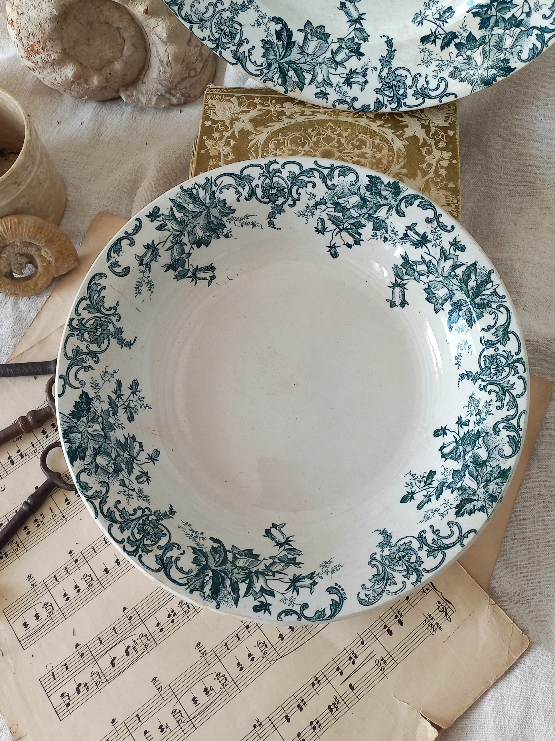 Decorative ceramic plate with green floral pattern on a surface with music sheet and shells.