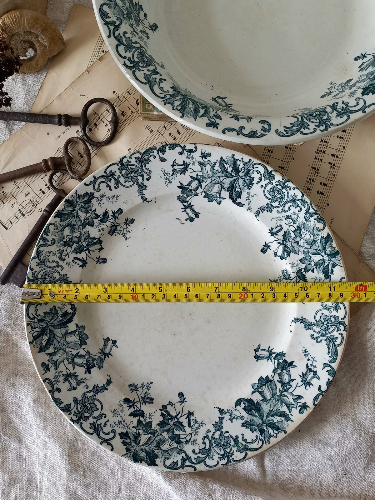 Decorative plates with green floral patterns on a surface with a measuring tape.