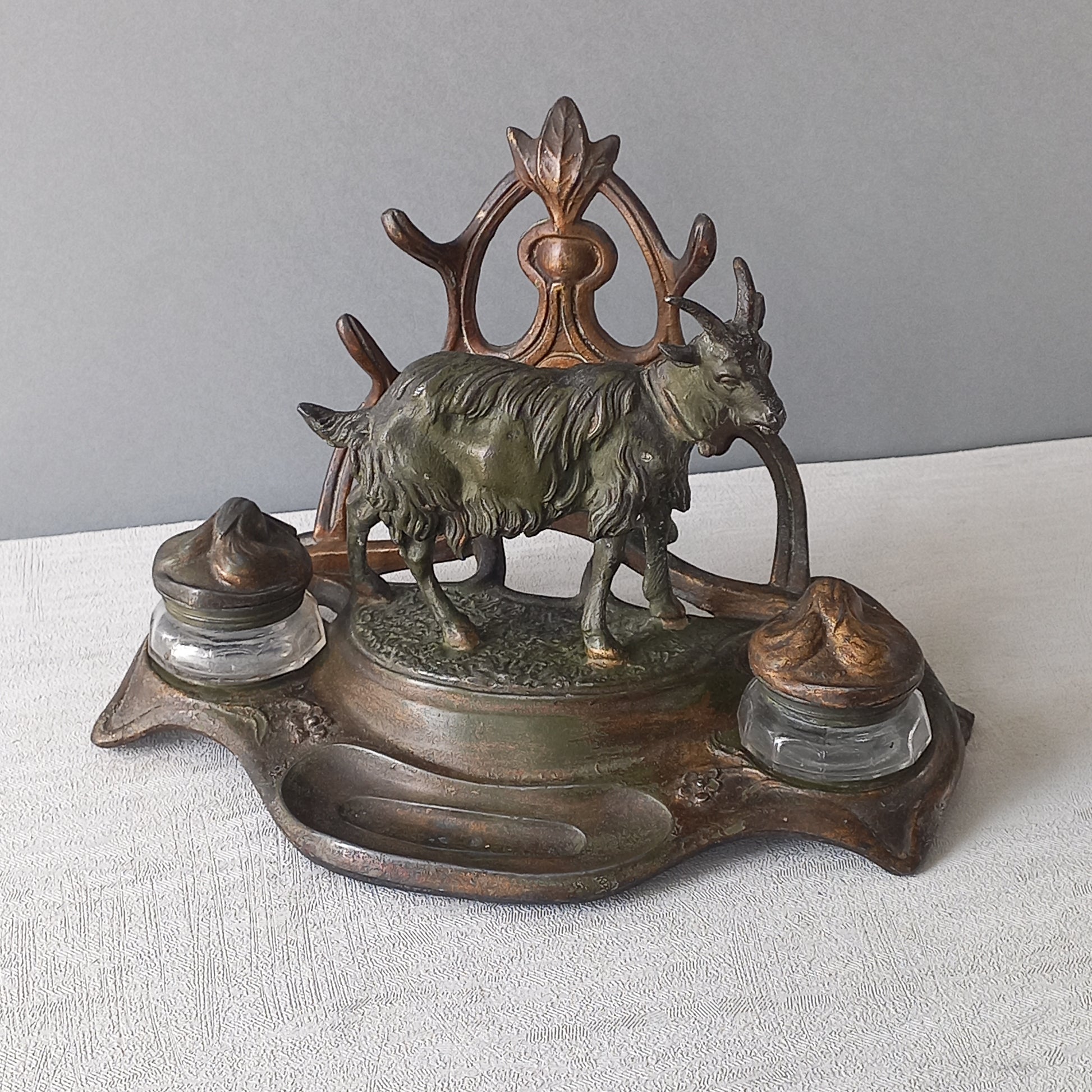 A stunning French art nouveau double inkwell with a goat figurine.

This wonderful antique inkwell has been sculpted in metal and signed by the artist (see photos). Behind the beautiful goat figurine are two pen rests and either side of the goat are two small glass ink pots with decorative metal lids.

The metal is finished in a lovely shade of green that has worn over time with traces of gold colour beneath - it has a wonderful patina of time all over it.