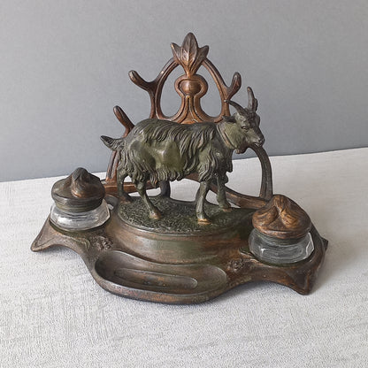 A stunning French art nouveau double inkwell with a goat figurine.

This wonderful antique inkwell has been sculpted in metal and signed by the artist (see photos). Behind the beautiful goat figurine are two pen rests and either side of the goat are two small glass ink pots with decorative metal lids.

The metal is finished in a lovely shade of green that has worn over time with traces of gold colour beneath - it has a wonderful patina of time all over it.