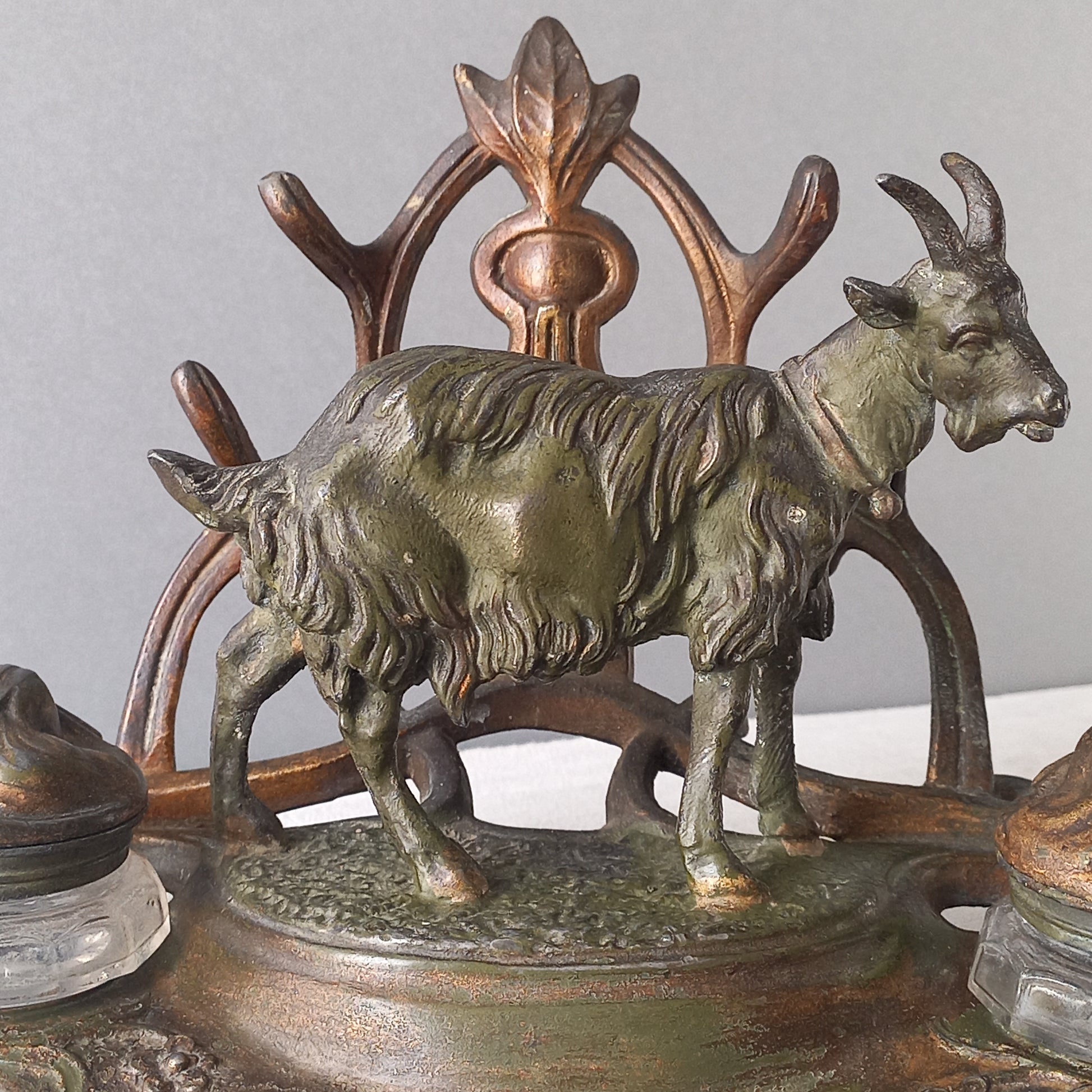 A stunning French art nouveau double inkwell with a goat figurine.

This wonderful antique inkwell has been sculpted in metal and signed by the artist (see photos). Behind the beautiful goat figurine are two pen rests and either side of the goat are two small glass ink pots with decorative metal lids.

The metal is finished in a lovely shade of green that has worn over time with traces of gold colour beneath - it has a wonderful patina of time all over it.