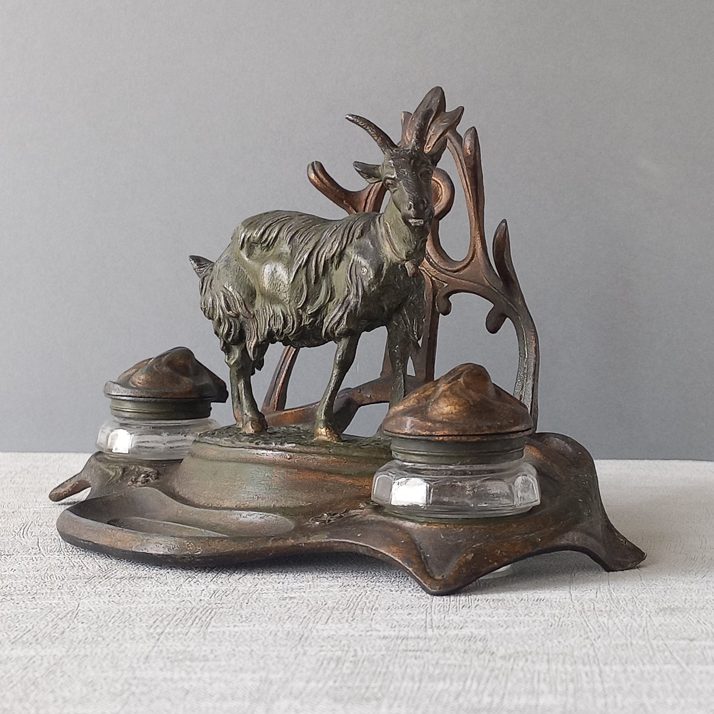 A stunning French art nouveau double inkwell with a goat figurine.

This wonderful antique inkwell has been sculpted in metal and signed by the artist (see photos). Behind the beautiful goat figurine are two pen rests and either side of the goat are two small glass ink pots with decorative metal lids.

The metal is finished in a lovely shade of green that has worn over time with traces of gold colour beneath - it has a wonderful patina of time all over it.