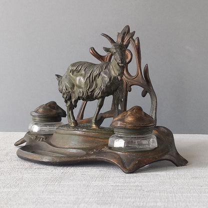 A stunning French art nouveau double inkwell with a goat figurine.

This wonderful antique inkwell has been sculpted in metal and signed by the artist (see photos). Behind the beautiful goat figurine are two pen rests and either side of the goat are two small glass ink pots with decorative metal lids.

The metal is finished in a lovely shade of green that has worn over time with traces of gold colour beneath - it has a wonderful patina of time all over it.