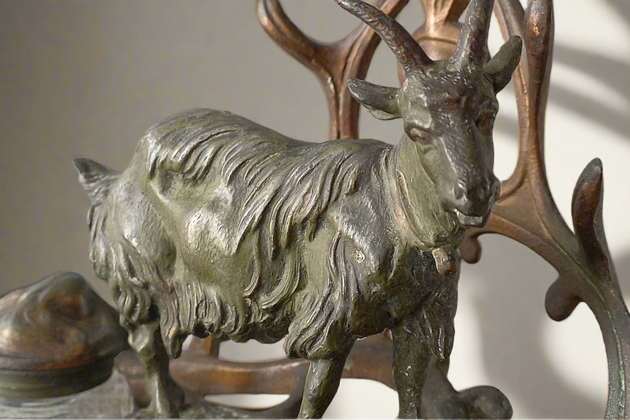 A stunning French art nouveau double inkwell with a goat figurine.

This wonderful antique inkwell has been sculpted in metal and signed by the artist (see photos). Behind the beautiful goat figurine are two pen rests and either side of the goat are two small glass ink pots with decorative metal lids.

The metal is finished in a lovely shade of green that has worn over time with traces of gold colour beneath - it has a wonderful patina of time all over it.