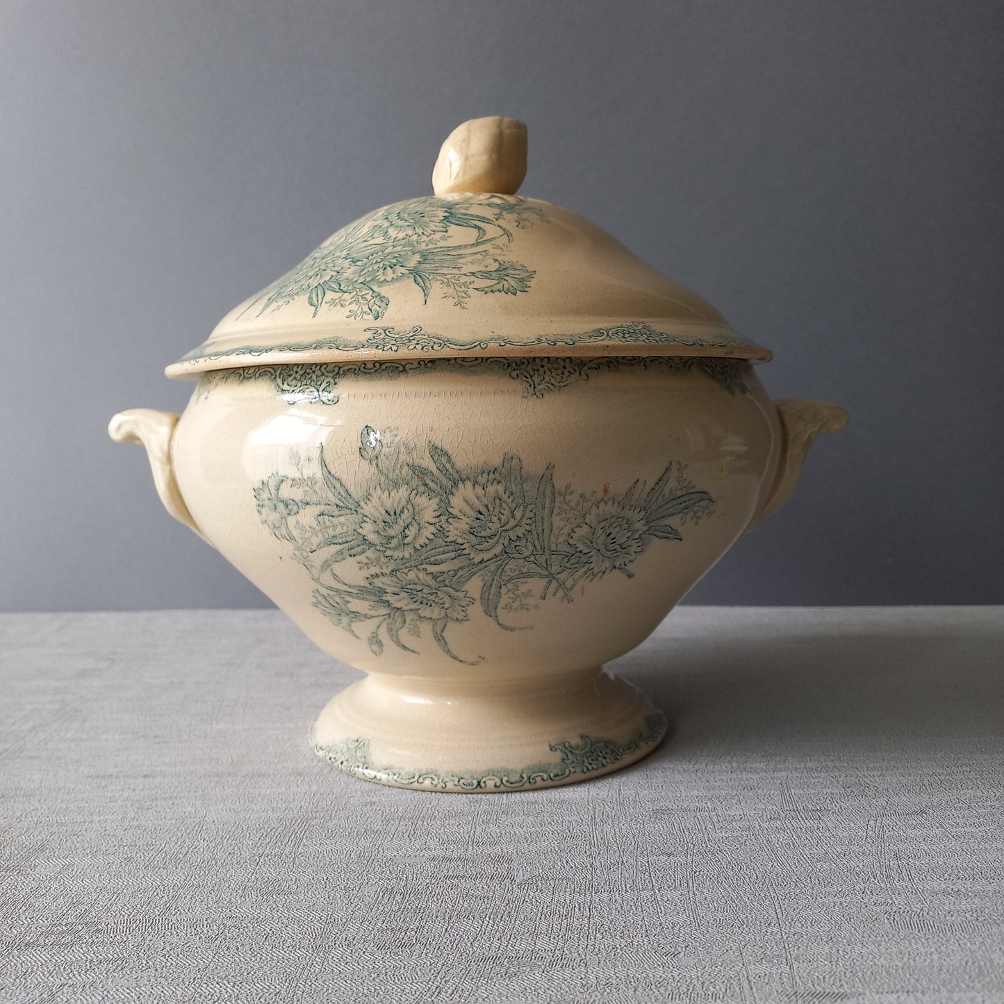 A pretty antique ironstone soup tureen with aged and faded floral transfer pattern in a beautiful shade of blue green or teal. Over time this wonderful old tureen has developed a pleasing faded creamy white finish. In summary, a beautiful piece of authentic antique ironstone from France.
